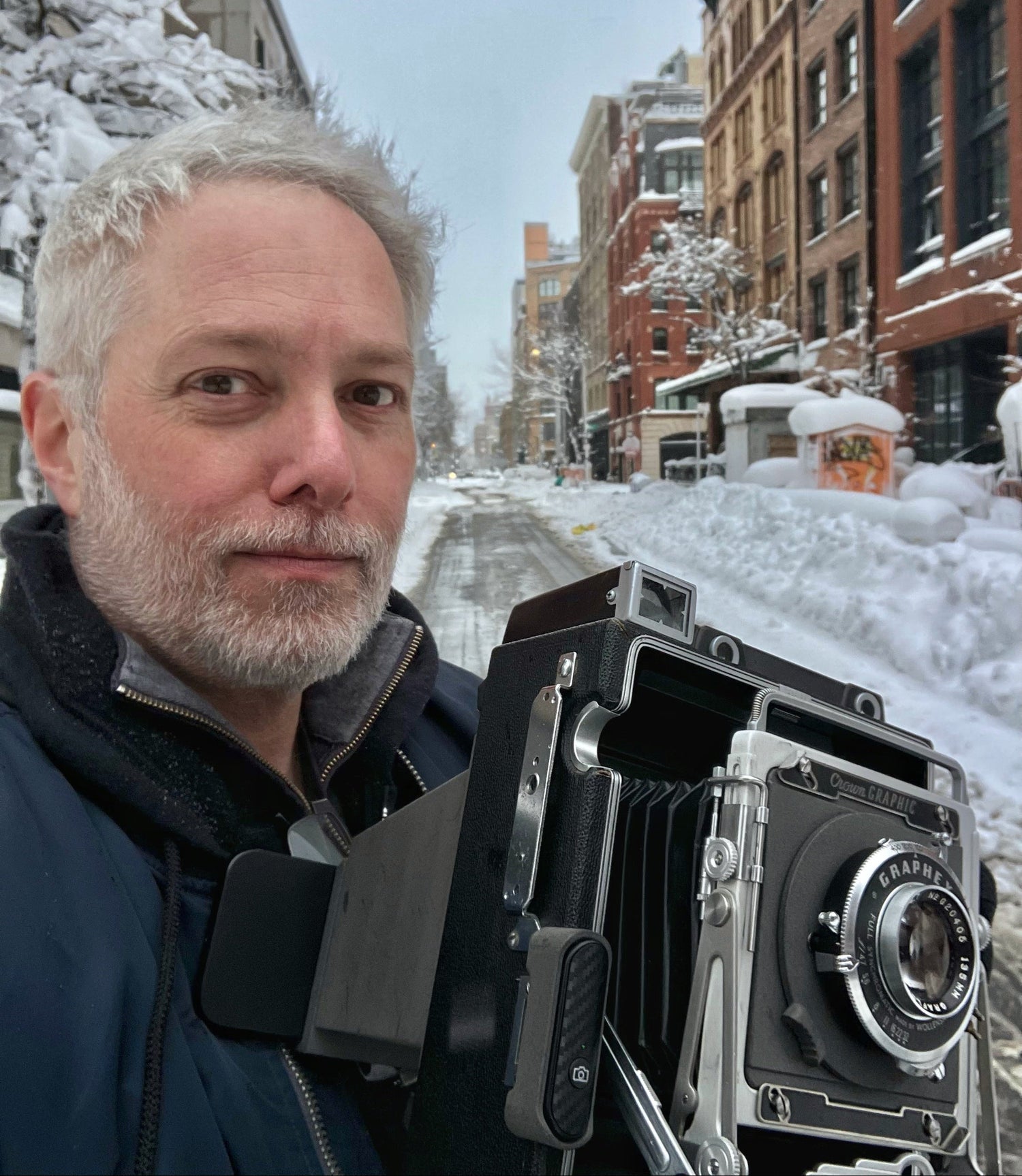 Toby Wilkins holding a vintage Graflex 4x5 camera fitted with his ObscuraFlex digital adapter on a snowy city street in New York City 2026. 
